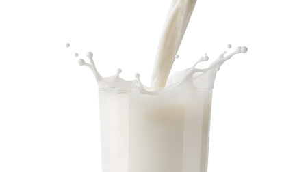 A close-up shot captures milk being poured into a clear glass, creating a dynamic splash and droplets. The white liquid contrasts against a black background, highlighting the motion and texture of the pour.の写真素材