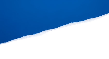 A close-up view of a torn paper edge, creating a diagonal line across the frame. The upper portion reveals a vibrant blue sky, while the lower portion is a solid black background. The torn edge is white and textured.の写真素材