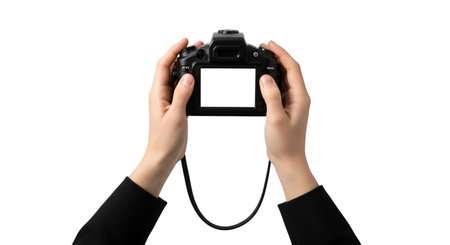 A pair of hands, wearing a black sleeve on the left arm, holds a black DSLR camera. The camera's LCD screen is bright white and blank, facing the viewer. A black camera strap is attached to the camera and dangles downwards. The background is solid black.の写真素材