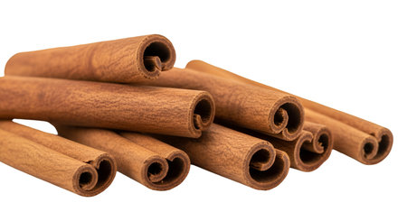 A close-up view of several rolled cinnamon sticks piled together against a dark background. The...