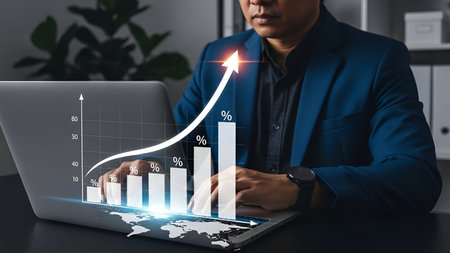 A man in a blue suit is seated at a desk, analyzing a digital bar chart on a laptop screen. The...