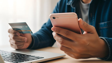 The a person wearing a blue jacket holding a credit card in one hand and a pink smartphone in the...