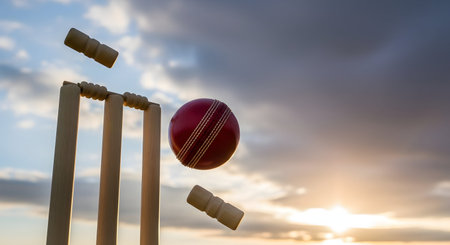 Outdoor showing cricket ball hitting wicket at sunset keywords: cricket, cricket ball, wicket, stumps, bails, sport, game, action, motion, sunset, sky, clouds, sports, recreation, competition, play, outdoor, field, pitch, boundary, fast, impact, hit, strike, dramatic, golden hour, evening, athletic, equipment, wooden stumps, red ball, game play, match, tournament, victory, defeat description: a red cricket ball is captured in mid-air, having just struck a wooden cricket wicket, sending the...