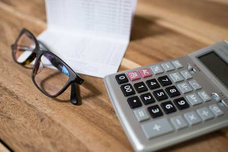 Workplace accountant. Notepad , calculator, and glasses on a wooden table in the background of a stack of books.の写真素材