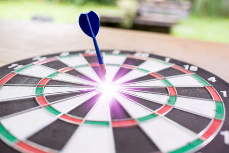 Blue dart arrow hitting in the target center of dartboard with green background,with business conceptの写真素材