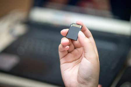 Woman copying photos from her camera to laptop. Hand with SD card.の写真素材