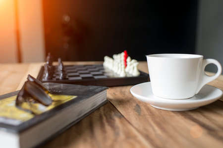 a cup of coffee with blurred Chess on the chessboard and glasses on bookの写真素材