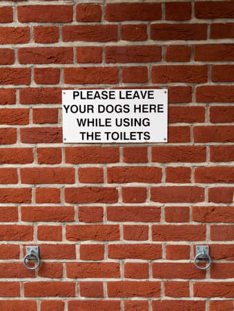 Comical please leave your dogs here while using the toilets sign outside public conveniencesのeditorial素材