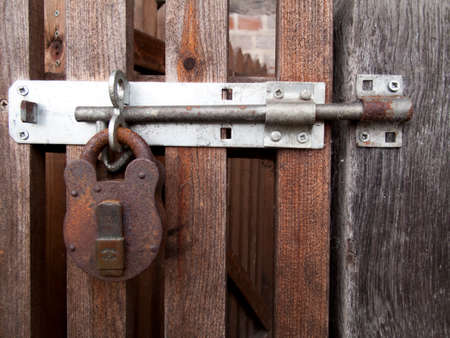 Rusty padlock clasp and staple securing timber gate to side of residential buildingの写真素材