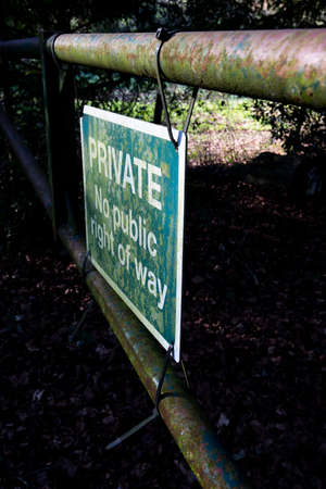 Private no right of way sign on old rusty metal gate blocking access to woodland countryside track with shallow depth of fieldの写真素材