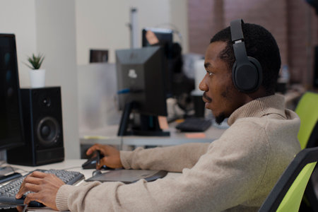African American designer in headphones draws on tablet 3D models for games.