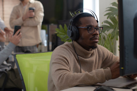 African American designer in headphones draws on tablet 3D models for games.