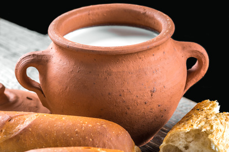 Clay pot with milk and baguette on a wooden tableの写真素材