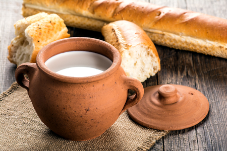 Clay pot with milk and baguette on a wooden tableの写真素材