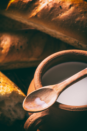 Clay pot with milk and baguette on a wooden tableの写真素材