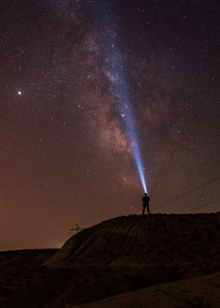 Milky Way on night sky and standing man silhouette with flashlight. Colorful night landscape. Exploring the universeの写真素材