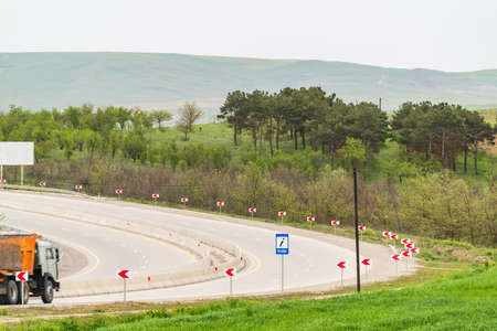 An empty highway with a sharp turn through green forest and hills
