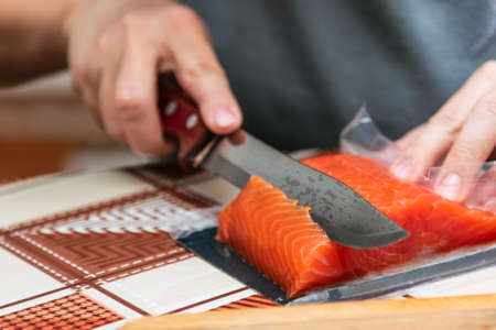 Hand with a knife cuts red salmon fish for sushi