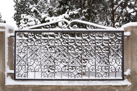metal fence in the snow on a background of trees in the parkの写真素材