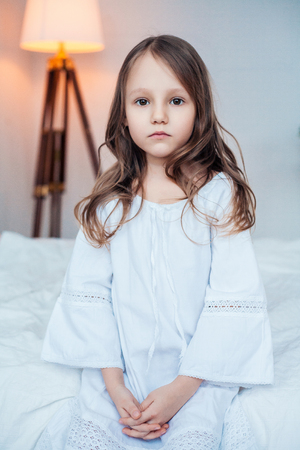 Cute little girl wearing nightgown sitting on the bed.の写真素材