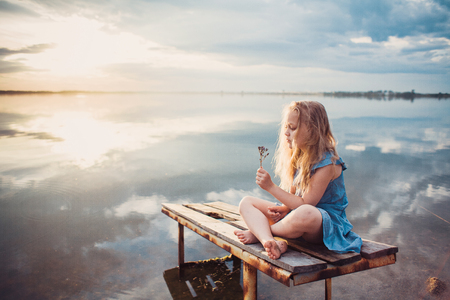 Cute child girl sitting on a wooden platform by the lake.の写真素材