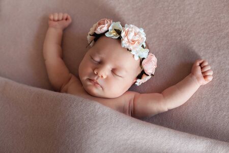 Cute newborn baby girl wearing flower headband peacefully sleeps in funny position.