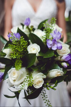 Close-up photo of wedding bouquet in bride's hands. White and purple flowers. Vertical image.の写真素材