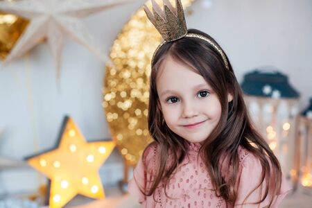 Smiling child girl wearing golden crown posing against christmas decorations.の写真素材