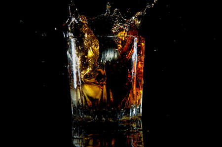 Drink with splash from ice cubes on black background vertical style