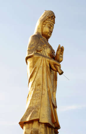 A golden statue of a Buddha against blue skyの写真素材