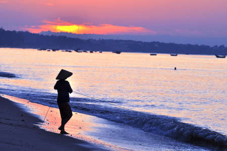 Silhouette of a fisherman on beach at sunriseの写真素材