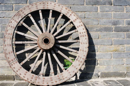 Ancient carriage wheel against brick wallの写真素材