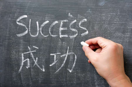 Success - word written with chalk on a blackboard with a Chinese translation, with a hand holding chalkの写真素材