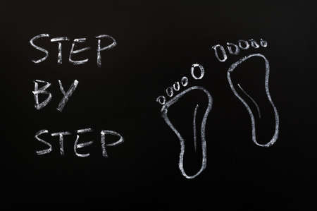 Footprints and the words step by step drawn with white chalk on a blackboardの写真素材