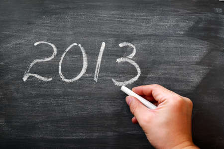 2013 written in chalk on a smudged blackboard,with a hand holding chalk