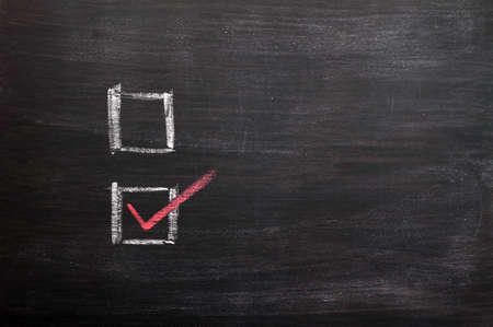 Check boxes with a red tick written with chalk on a smudged blackboardの写真素材