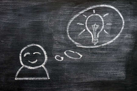 Speech bubble with a cartoon figure and innovation bulb drawn on a blackboard backgroundの写真素材