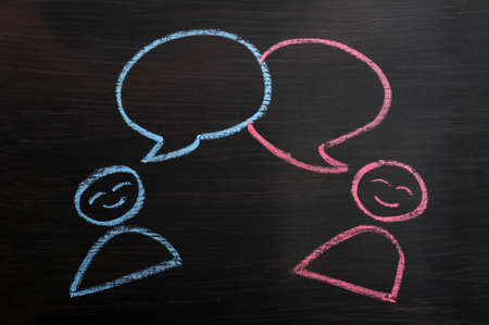 Chalk drawing of blank speech bubbles with human figures on a blackboard backgroundの写真素材