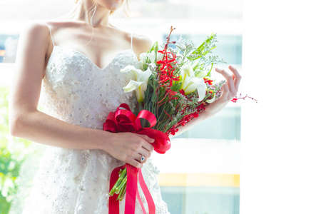 Women blonde hair wear wedding blue rings in white wedding dress. Holds a red and white bouquet and...
