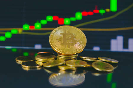 Close up of Golden bitcoin in front of stock chart in tablets on the glass floor. Dark, bokeh, blurred concept.の写真素材