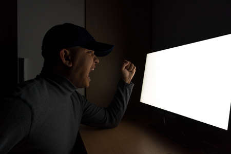 Side view of man Hacker sit at the computer monitor and angry and upset feeling in the dark room.