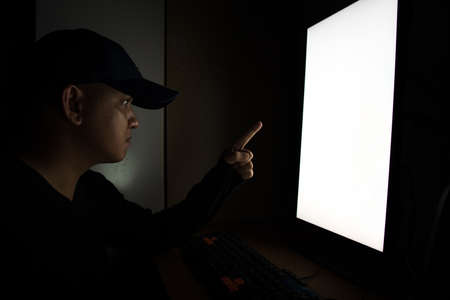 Side view of man Hacker sit at the computer monitor Pointing fingers monitor in the dark room.