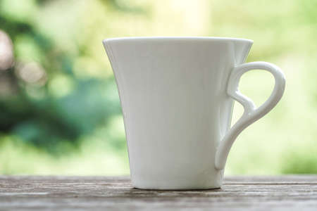 white coffee / tea mug on a wooden table against green bokeh backgroundの写真素材