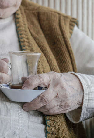 wrinkled hand of a senior woman holding a tea / coffee glassの写真素材