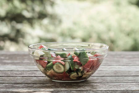 Mixed fresh salad on a wooden table against bokeh green backgroundの写真素材