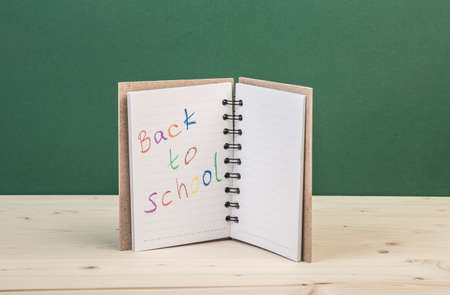 back to school template with a notebook on a wooden table against greenの写真素材
