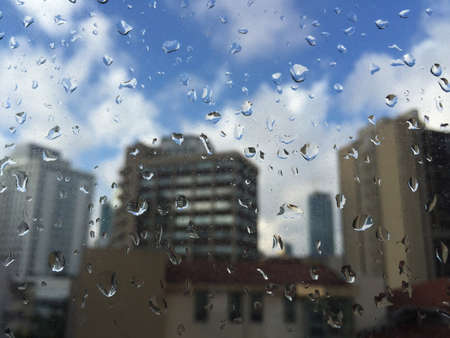rain drops on windowpane against buildings under blue skyの写真素材