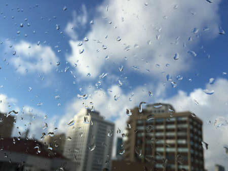 rain drops on windowpane against buildings under blue sky