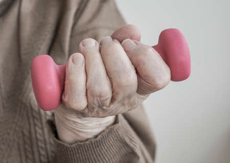 closeup wrinkled hand of a senior woman holding dumbbellの写真素材