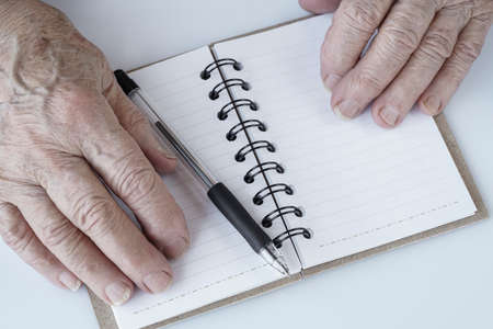 Closeup of Wrinkled hands and pencil on an empty notebookの写真素材